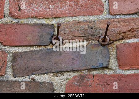 Zwei (2) rostige Nägel an alten roten Ziegelwänden. Texturierter Hintergrund aus Mauerwerk auf altem Gebäude. Ziegel sind ungleichmäßig verlegt. Stockfoto