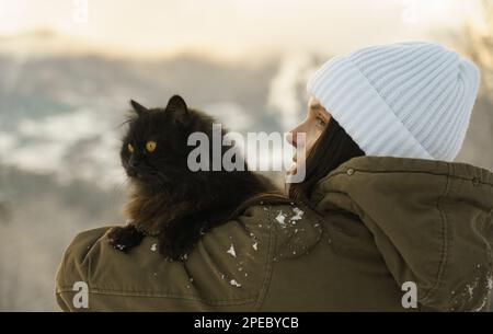 Eine Frau mit weißem Hut, die eine schwarze Katze draußen hält Stockfoto