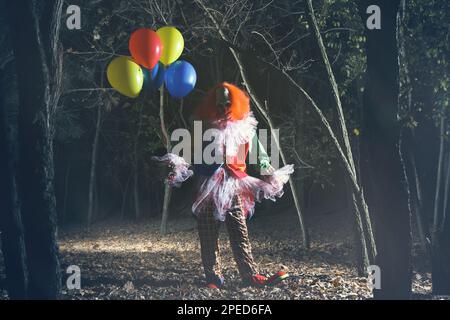 Furchteinflößender Clown mit Luftballons draußen in der Nacht. Halloween-Party-Kostüm Stockfoto