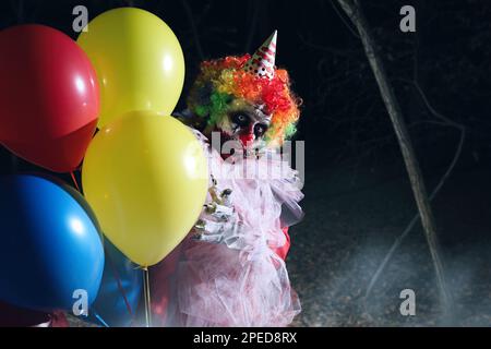 Furchteinflößender Clown mit Luftballons draußen in der Nacht. Halloween-Party-Kostüm Stockfoto