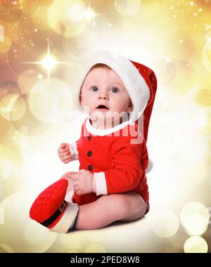 Süßes kleines Baby im Weihnachtsmann-Kostüm vor verschwommenen festlichen Lichtern. Weihnachtsfeier Stockfoto