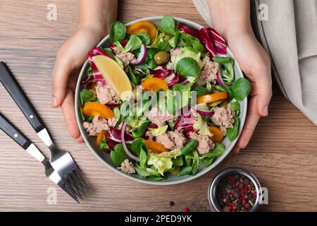 Frau mit Schüssel mit köstlichem Salat und Thunfischkonserven am Holztisch, Draufsicht Stockfoto