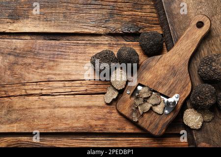 Rasierer mit ganzen und geschnittenen schwarzen Trüffeln auf einem Holztisch, flach liegend. Platz für Text Stockfoto