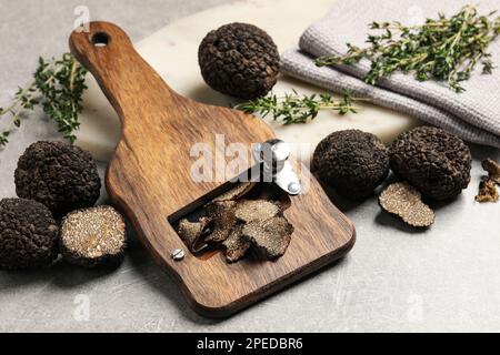 Frische schwarze Trüffel, Scheibe und Thymian auf grauem Tisch Stockfoto