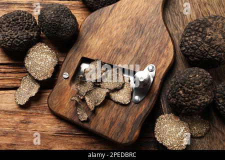 Rasierer mit ganzen und geschnittenen schwarzen Trüffeln auf einem Holztisch, flach liegend Stockfoto