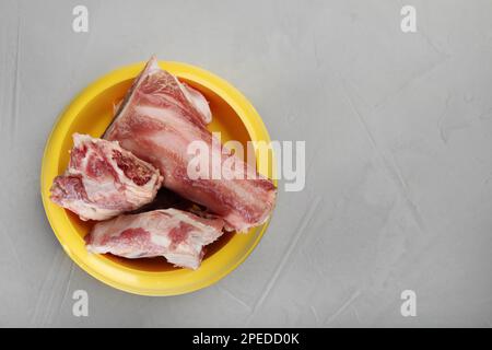 Fütterschüssel mit rohen gehackten Fleischknochen auf grauem Tisch, Draufsicht. Platz für Text Stockfoto