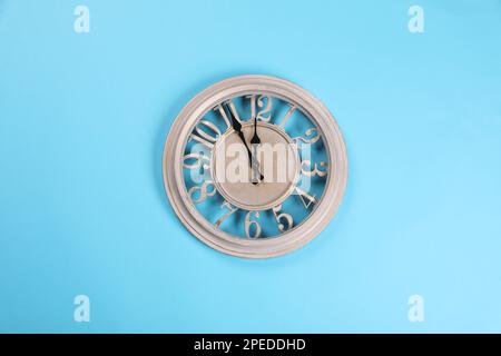 Die elegante Wanduhr zeigt fünf Minuten bis Mitternacht auf türkisfarbenem Hintergrund, Draufsicht. Der Countdown für das neue Jahr Stockfoto