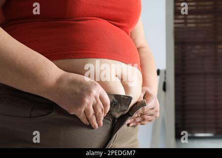 Übergewichtige Frau, die zu Hause enge Hosen zuknöpfen will, Nahaufnahme Stockfoto