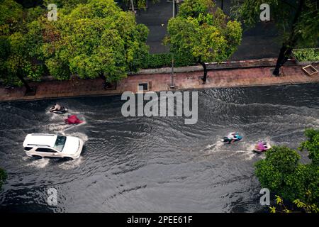 Straßenflut nach starkem Regen in einer asiatischen Stadt. Auto und Motorräder fahren in tiefem Wasser auf einer überfluteten Straße Stockfoto