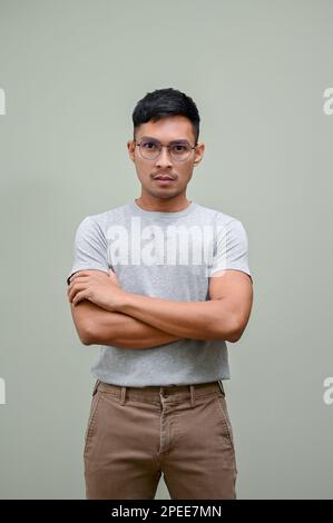 Gestresster und seriöser Asiate der Millennials in legerer Kleidung steht mit gekreuzten Armen vor einem isolierten grünen Hintergrund. Stockfoto