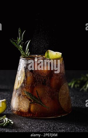 cola mit Limette und Eis auf dunklem Hintergrund. Dekoriert mit einem Zweig Rosmarin und einer Scheibe Limette Stockfoto