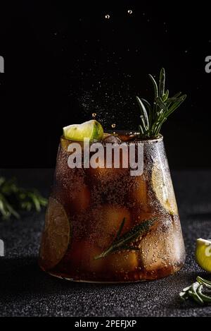 cola mit Limette und Eis auf dunklem Hintergrund. Dekoriert mit einem Zweig Rosmarin und einer Scheibe Limette Stockfoto