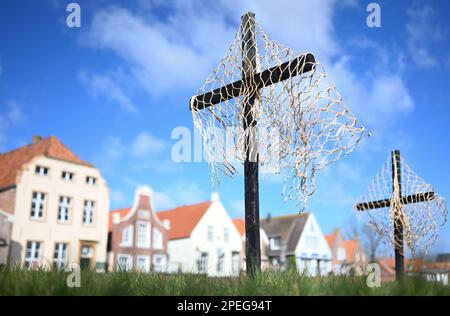 Greetsiel, Deutschland. 15. März 2023. Schwarze Kreuze mit Netzen sind ein stiller Protest der Fischer am Hafen. Die hölzernen Kreuze sollen zur Zeit die Aufmerksamkeit auf eine unmittelbare Gefahr an vielen Küstenorten in Norddeutschland lenken: Die Fischer haben sie errichtet, weil sie das Ende ihrer Industrie fürchten. Konkret geht es um ein geplantes Verbot von so genannten Grundschleppnetzen. Kredit: Lars Klemmer/dpa/Alamy Live News Stockfoto