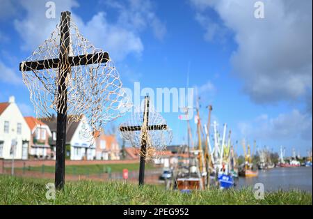 Greetsiel, Deutschland. 15. März 2023. Schwarze Kreuze mit Netzen sind ein stiller Protest der Fischer am Hafen. Die hölzernen Kreuze sollen zur Zeit die Aufmerksamkeit auf eine unmittelbare Gefahr an vielen Küstenorten in Norddeutschland lenken: Die Fischer haben sie errichtet, weil sie das Ende ihrer Industrie fürchten. Konkret geht es um ein geplantes Verbot von so genannten Grundschleppnetzen. Kredit: Lars Klemmer/dpa/Alamy Live News Stockfoto