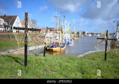 Greetsiel, Deutschland. 15. März 2023. Schwarze Kreuze mit Netzen sind ein stiller Protest der Fischer am Hafen. Die hölzernen Kreuze sollen zur Zeit die Aufmerksamkeit auf eine unmittelbare Gefahr an vielen Küstenorten in Norddeutschland lenken: Die Fischer haben sie errichtet, weil sie das Ende ihrer Industrie fürchten. Konkret geht es um ein geplantes Verbot von so genannten Grundschleppnetzen. Kredit: Lars Klemmer/dpa/Alamy Live News Stockfoto