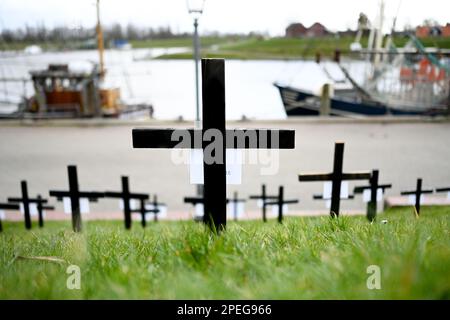 Greetsiel, Deutschland. 15. März 2023. Schwarze Kreuze sind ein stiller Protest der Fischer auf dem Deich im Hafen. Die hölzernen Kreuze sollen zur Zeit die Aufmerksamkeit auf eine unmittelbare Gefahr an vielen Küstenorten in Norddeutschland lenken: Die Fischer haben sie errichtet, weil sie das Ende ihrer Industrie fürchten. Konkret geht es um ein geplantes Verbot von so genannten Grundschleppnetzen. Kredit: Lars Klemmer/dpa/Alamy Live News Stockfoto