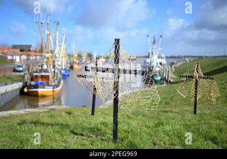 Greetsiel, Deutschland. 15. März 2023. Schwarze Kreuze sind ein stiller Protest der Fischer auf dem Deich im Hafen. Die hölzernen Kreuze sollen zur Zeit die Aufmerksamkeit auf eine unmittelbare Gefahr an vielen Küstenorten in Norddeutschland lenken: Die Fischer haben sie errichtet, weil sie das Ende ihrer Industrie fürchten. Konkret geht es um ein geplantes Verbot von so genannten Grundschleppnetzen. Kredit: Lars Klemmer/dpa/Alamy Live News Stockfoto