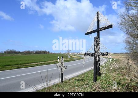 Greetsiel, Deutschland. 15. März 2023. Schwarze Kreuze mit Netzen sind ein stiller Protest von Krabbenfischern auf einer Landstraße in Krummhörn. Die hölzernen Kreuze sollen zur Zeit die Aufmerksamkeit auf eine drohende Gefahr in vielen Küstenstädten in Norddeutschland lenken: Die Fischer haben sie errichtet, weil sie das Ende ihrer Industrie fürchten. Konkret geht es um ein geplantes Verbot von so genannten Grundschleppnetzen. Kredit: Lars Klemmer/dpa/Alamy Live News Stockfoto