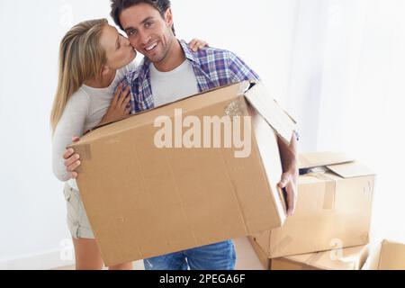 Ihre Dankbarkeit zum Ausdruck zu bringen. Porträt eines gutaussehenden jungen Mannes, der lächelt und eine Schachtel trägt, während seine Freundin ihn auf die Wange küsst. Stockfoto