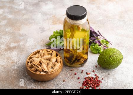 Sonnenblumenöl in einem Glasgefäß mit verschiedenen Kräutern und Gewürzen, Sesam, Rosmarin, Avocado, Basilikum, Mandel auf braunem Betonhintergrund. Seitenansicht, Kopie en Stockfoto