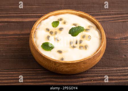 Joghurt mit Granadilla und Minze in einer Holzschüssel auf braunem Holzhintergrund. Seitenansicht, Nahaufnahme. Stockfoto