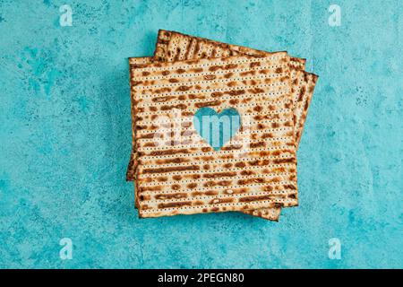 Pesach-Festungskonzept - jüdischer Feiertag Pesach. Matzah-Quadrate, gestapelt in einem Quadrat auf blauem Hintergrund. Das Herz ist in Matzah geschnitzt. Flach verlegt. Stockfoto