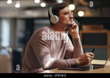 Webdesigner denkt über sein Projekt nach, während er in einem Café sitzt. Freiberuflicher Designexperte, der mit einem Grafiktablett und einem Notebook arbeitet. Stockfoto