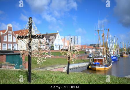 Greetsiel, Deutschland. 15. März 2023. Schwarze Kreuze mit Netzen sind ein stiller Protest der Fischer am Hafen. Die hölzernen Kreuze sollen zur Zeit die Aufmerksamkeit auf eine unmittelbare Gefahr an vielen Küstenorten in Norddeutschland lenken: Die Fischer haben sie errichtet, weil sie das Ende ihrer Industrie fürchten. Konkret geht es um ein geplantes Verbot von so genannten Grundschleppnetzen. Kredit: Lars Klemmer/dpa/Alamy Live News Stockfoto