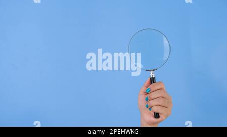 Weibliche Hände halten Lupe auf pastellblauem Hintergrund im Studio. Körpersprachbegriff. Mit Platz für Text oder Bild, Werbeinhalt. Stockfoto