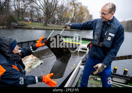 Berlin, Deutschland. 13. März 2023. Andreas Müller (r) und Stephan Strauch, Mitarbeiter der Wasser- und Schifffahrtsbehörde, laden während einer Bootsfahrt einen aus dem Wasser gezogenen Stuhl auf einen schwimmenden Container, um Hindernisse im Landwehrkanal zu beseitigen. Fahrräder, Teppiche, Leihroller, Stühle, Kleidung - alles endet in Berlins Landwehrkanal und macht viel Arbeit, wenn es um die Reinigung geht. Bei einigen Fundstücken wird die Polizei gerufen. (Dpa 'mit Bootshaken und Sounding-Rahmen: Auf der Spur der Wasserverschwendung') Credit: Monika Skolimowska/dpa/Alamy Live News Stockfoto