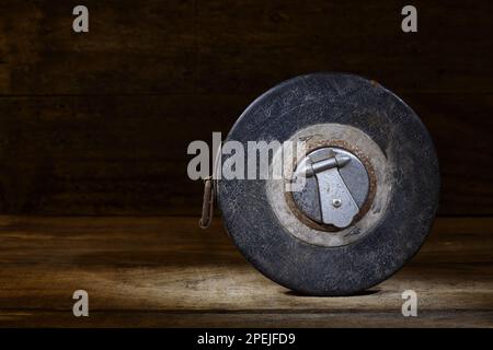 Ein schwarzes, klassisches, aufziehbares, zölliges Maßband aus Metall auf rustikalem Holz in sanfter, dunkler Stimmungsbeleuchtung, das in einem Studio aufgenommen wurde Stockfoto