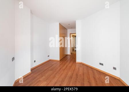 Asymmetrischer weißer Flur, der an einem Kleiderschrank mit holzfarbenem Laminatboden vorbei zum Ausgang führt. Konzept einer ungewöhnlichen Gestaltung einer Wohnung oder Stockfoto