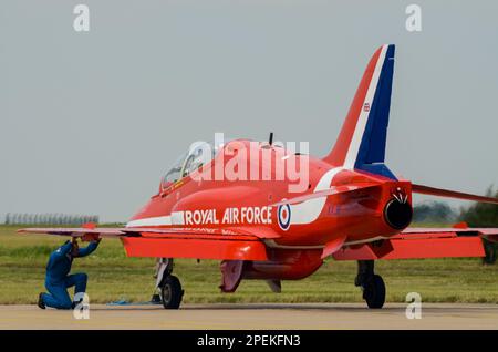 Die Roten Pfeile der Royal Air Force zeigen das Team BAE Hawk T1 Düsenflugzeug, das auf der RAF Scampton ausgestellt wird, wobei ein Bodenbesatzungsmitglied unter dem Flügel nachsieht Stockfoto