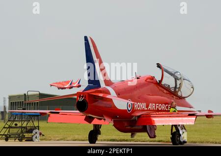 Die Roten Pfeile der Royal Air Force zeigen das Team BAE Hawk T1-Düsenflugzeuge, die auf der RAF Scampton über einem Ersatzjet und einem Bodentechniker ausgestellt werden Stockfoto