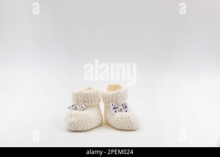 Gestrickte weiße Babyschühchen mit Schleifen mit Punktmuster auf einem grau isolierten Hintergrund. Hintergrund. Für Text. Foto in hoher Qualität Stockfoto