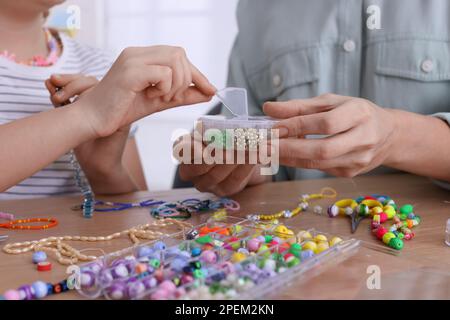 Mutter mit ihrer Tochter, die zu Hause Perlenschmuck herstellt Stockfoto