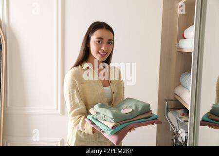 Schöne Frau mit Kleidung und einem duftenden Beutel in der Nähe des Kleiderschranks Stockfoto