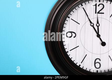 Stilvolle Wanduhr zeigt fünf Minuten bis Mitternacht auf türkisfarbenem Hintergrund an, Draufsicht mit Platz für Text. Der Countdown für das neue Jahr Stockfoto