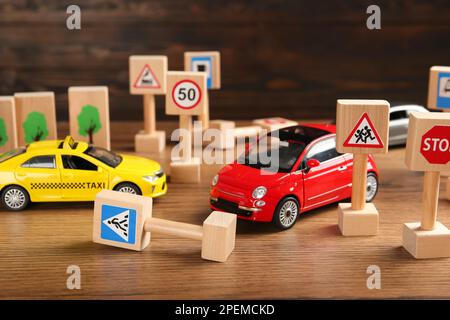 Verschiedene Miniatur-Straßenschilder und Autos auf Holztisch. Fahrschule Stockfoto