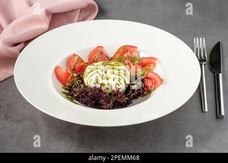 Burratakäse mit Tomaten und frischem Gemüse auf einer weißen Porzellanplatte Stockfoto