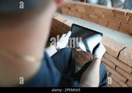 Der Baumeister steht im Haus im Bau und hält den Tablet-Computer Stockfoto