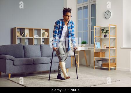 Behinderter junger afrikaner mit gebrochenem Bein, der versucht, mit Krücken zu gehen. Stockfoto