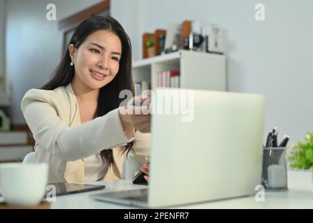 Wunderschöne asiatische Geschäftsfrau, die per Videokonferenz auf einem Laptop kommuniziert, während sie von zu Hause aus arbeitet Stockfoto