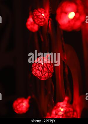 Rote Rattan-Kugel-Girlande an gemusterten Wänden. Weihnachts-LED-Lichter auf dunklem Hintergrund. Girlande der Glühbirne ist verschwommen. Nahaufnahme Stockfoto