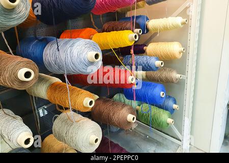 Spulen mit Fäden verschiedener Farben auf den Regalen einer Bekleidungsfabrik oder -Produktion. Lifestyle Stockfoto