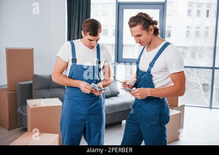 Ich habe Geld. Zwei junge Spielfiguren in blauer Uniform, die im Zimmer arbeiten Stockfoto