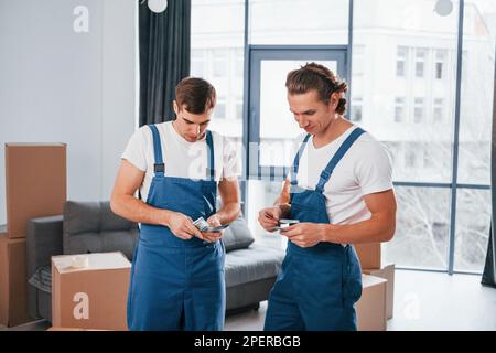 Ich habe Geld. Zwei junge Spielfiguren in blauer Uniform, die im Zimmer arbeiten Stockfoto