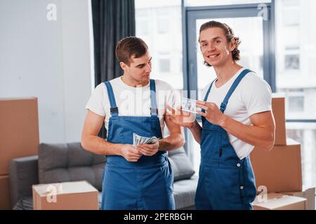 Ich habe Geld. Zwei junge Spielfiguren in blauer Uniform, die im Zimmer arbeiten Stockfoto