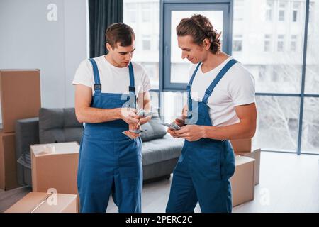 Ich habe Geld. Zwei junge Spielfiguren in blauer Uniform, die im Zimmer arbeiten Stockfoto
