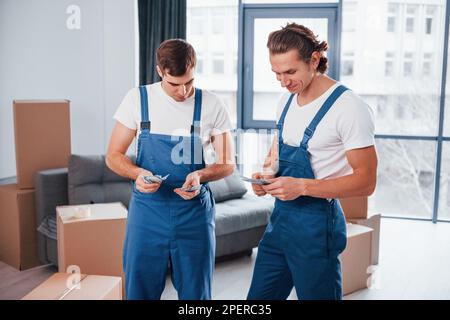 Ich habe Geld. Zwei junge Spielfiguren in blauer Uniform, die im Zimmer arbeiten Stockfoto